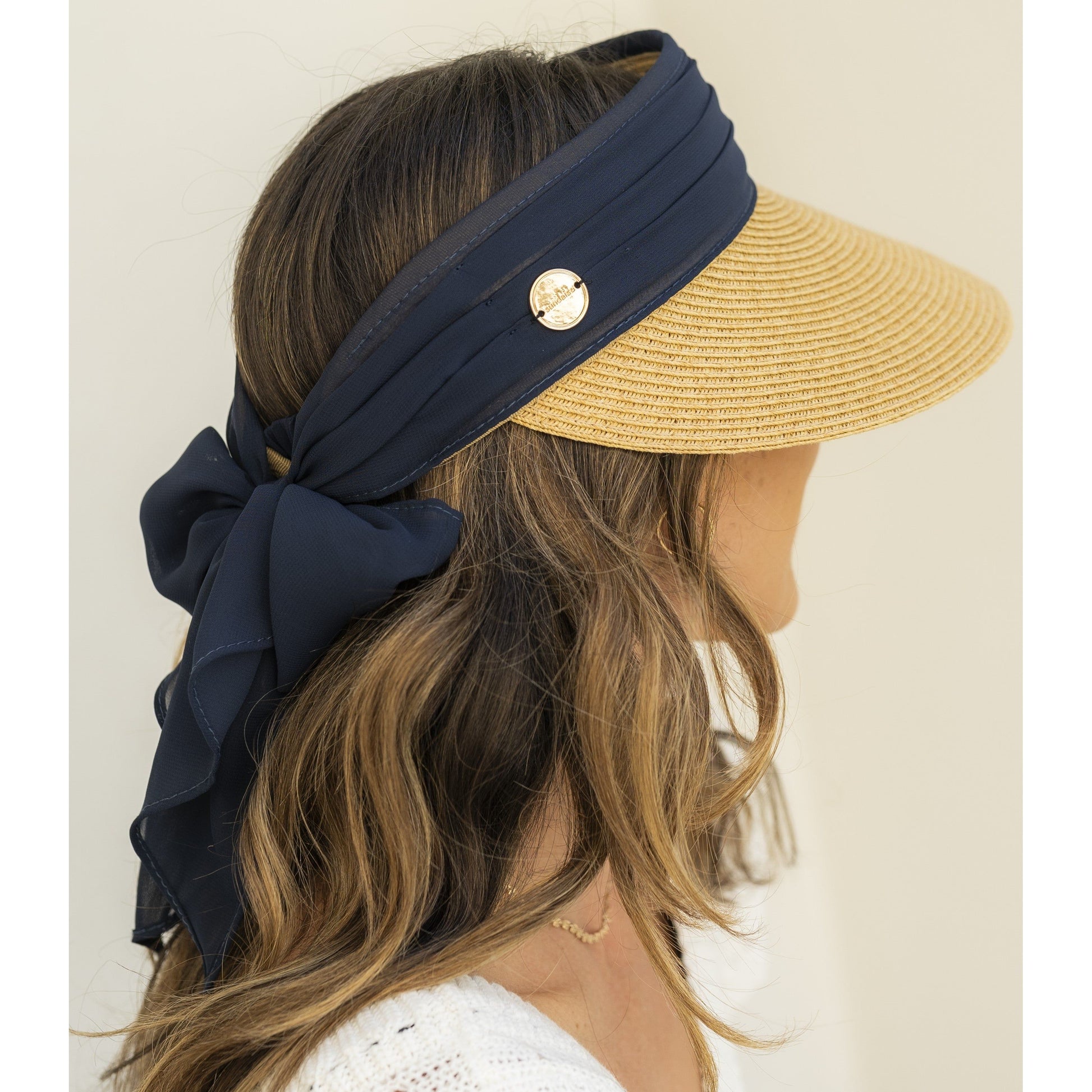 Woman wearing a straw visor with a navy headband and bow on a plain background