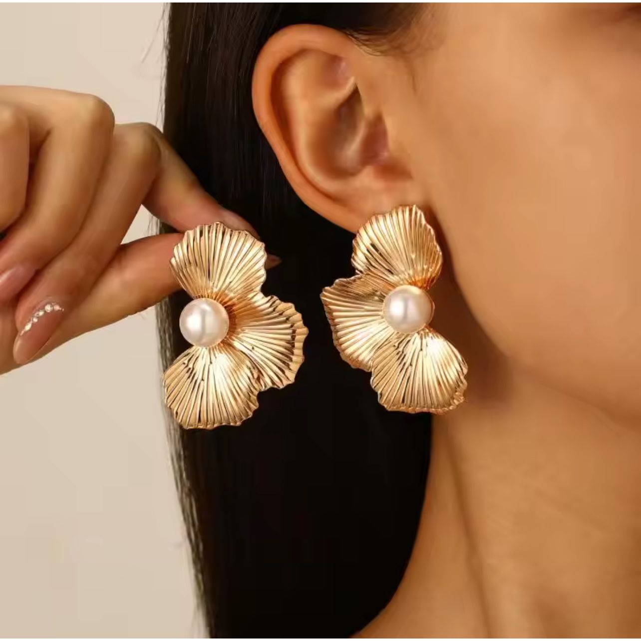 Gold earrings with pearl centers worn by a person against a neutral background