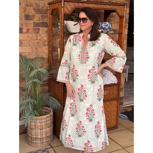 Woman wearing a floral dress standing in front of a wooden cabinet with plants.