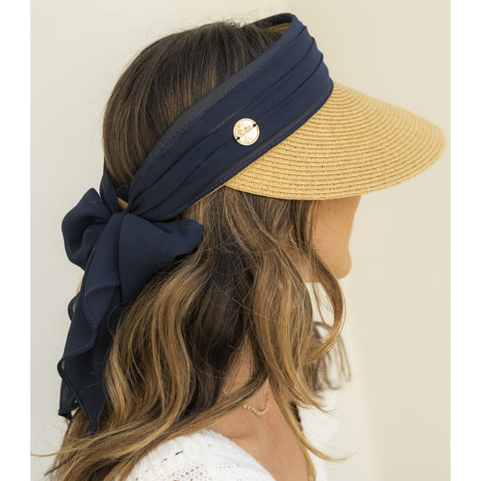 Woman wearing a straw visor with a navy headband and bow on a plain background